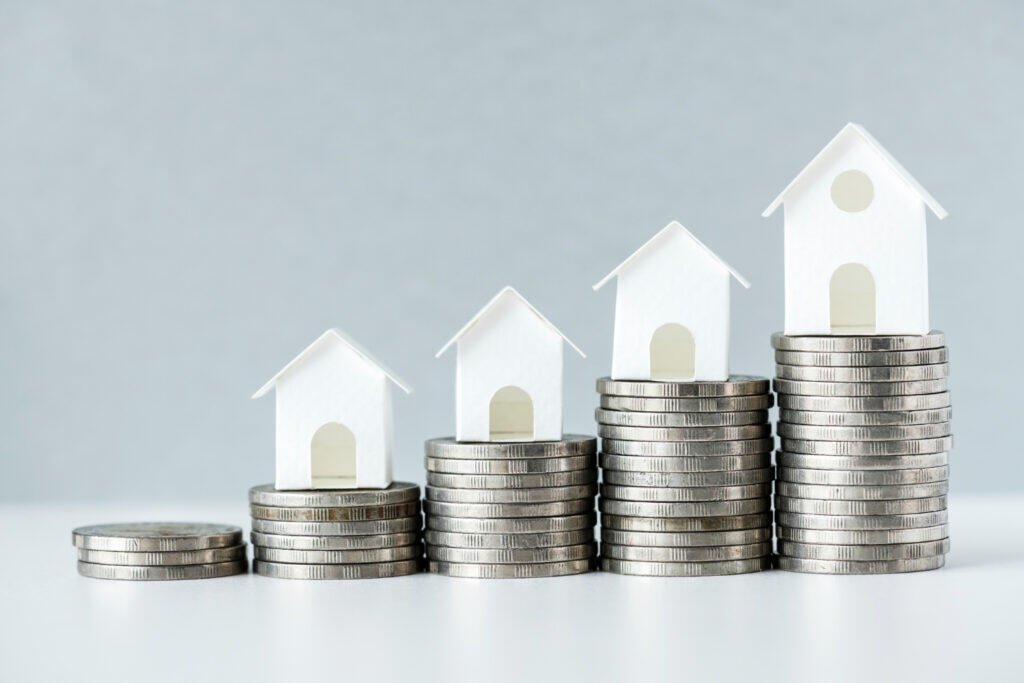 Growing stacks of coins with miniature houses on top, representing increasing home value or savings.