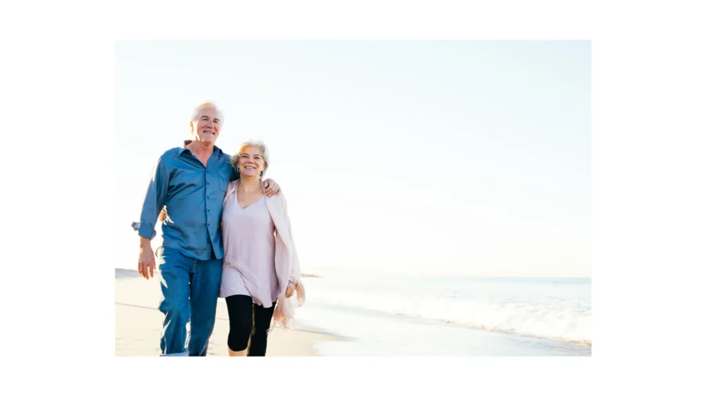 Happy retired couple walking on the beach, enjoying retirement planning.