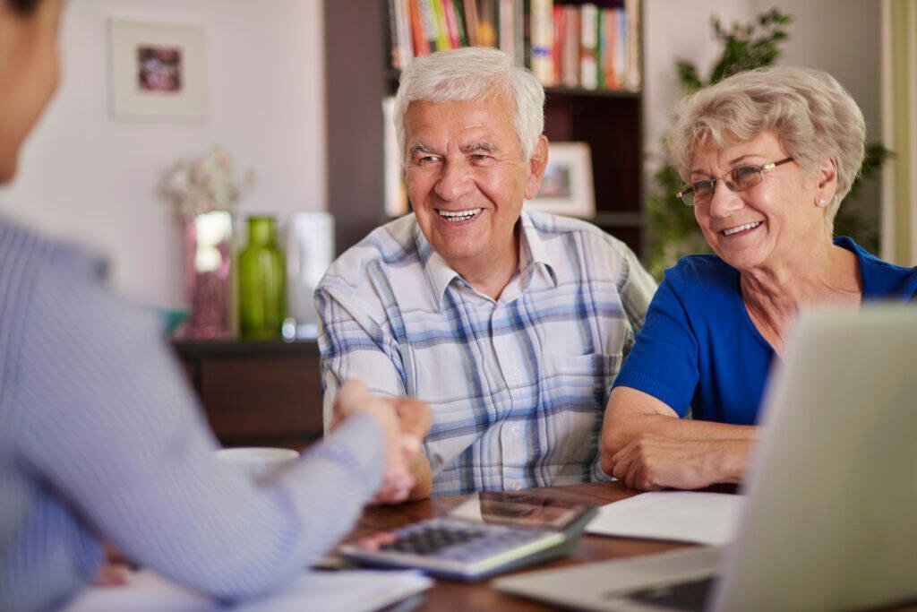 Happy senior couple shaking hands with financial advisor, discussing retirement planning costs.